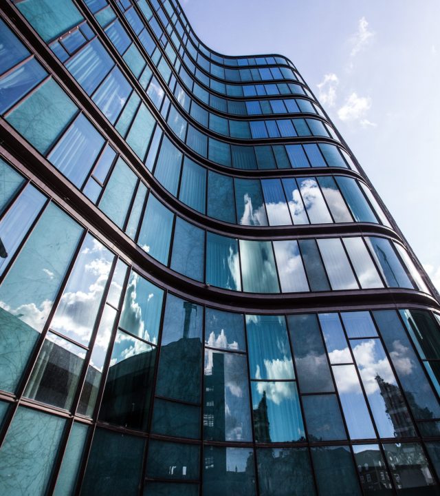 A vertical low angle shot of a high rise building in a glass facade with the reflection of the surrounding buildings
